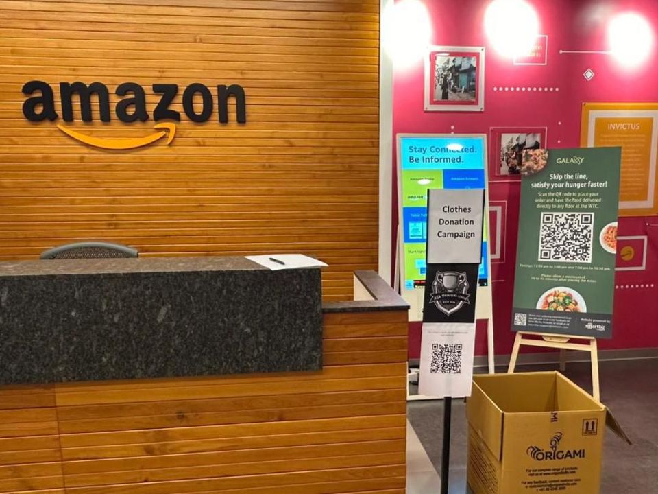 A clothes donation point with a QR code standee and a collection carton at an Amazon office reception in India